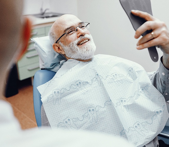 Older man in plaid shirt smiling with implant dentures