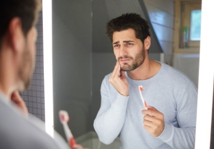Man looking in mirror and holding his cheek in pain